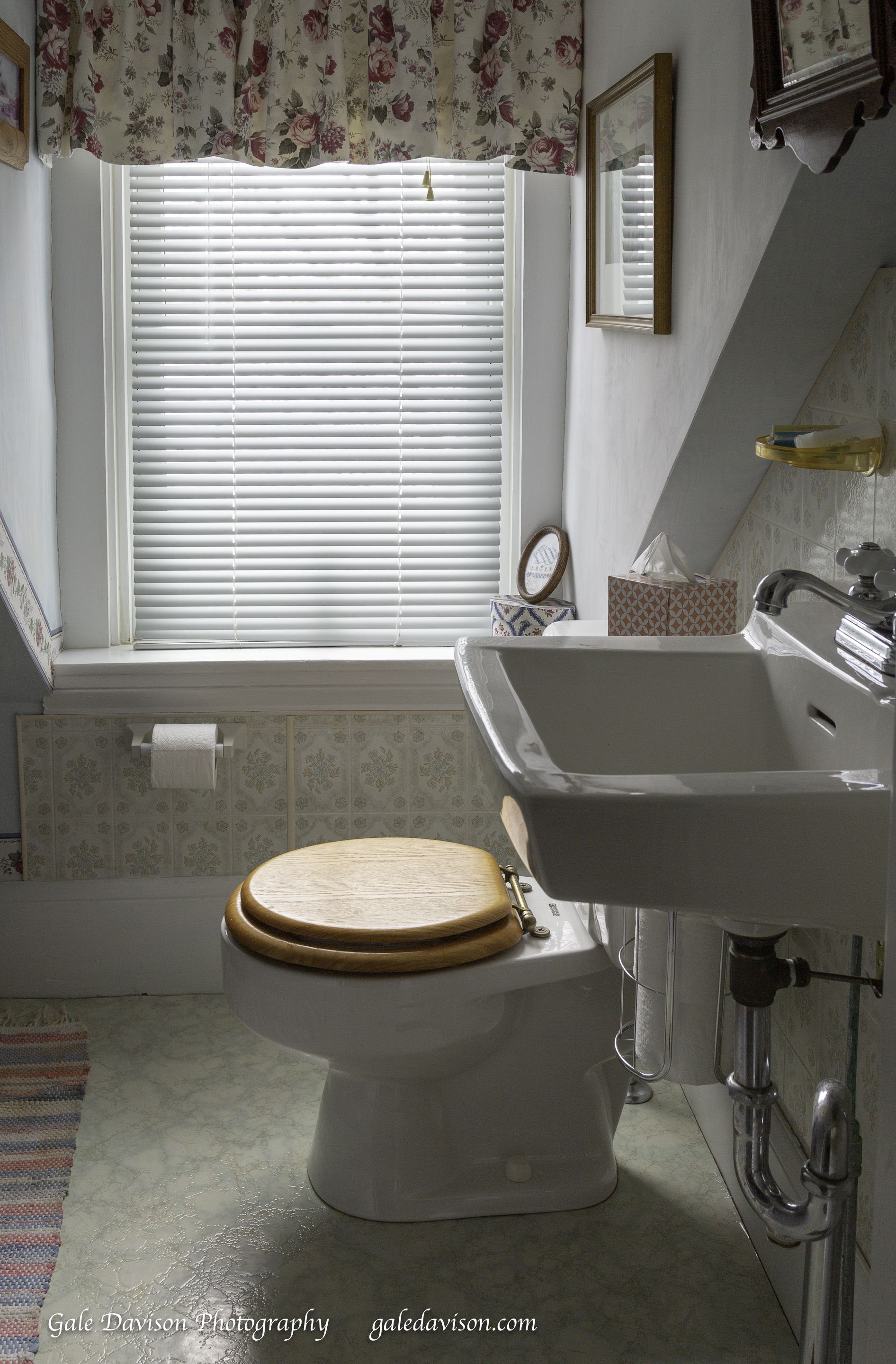 A bathroom with a toilet, sink, and window with blinds.