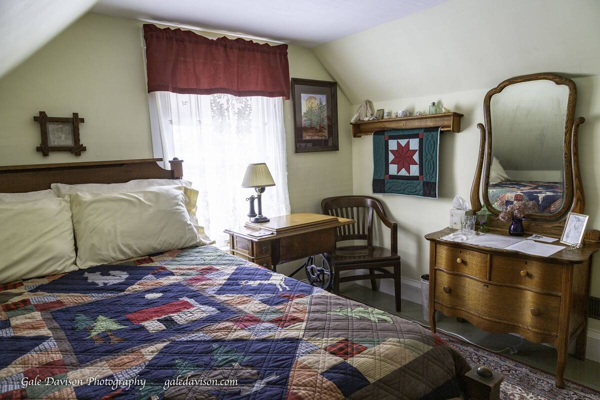 A bedroom with a large bed, a desk with a chair, a dresser, and a mirror.