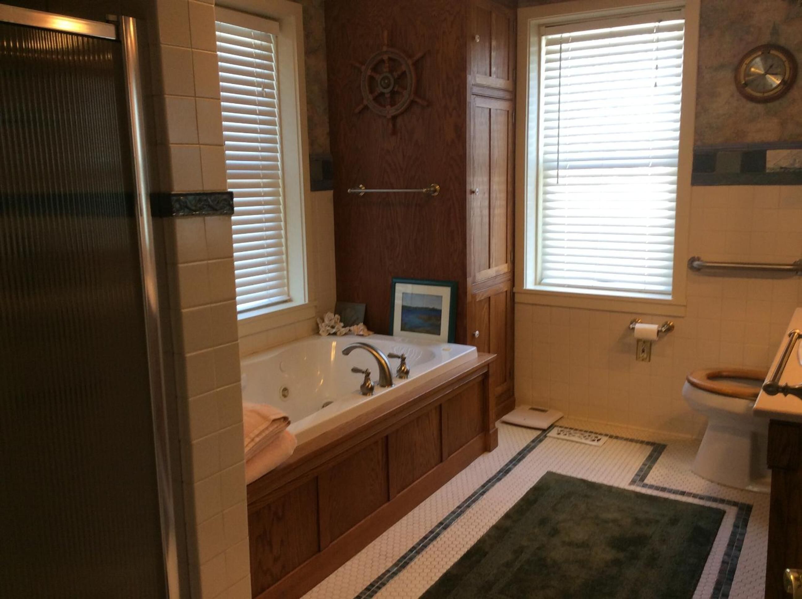 A bathroom with a bathtub, toilet, and a window with blinds.