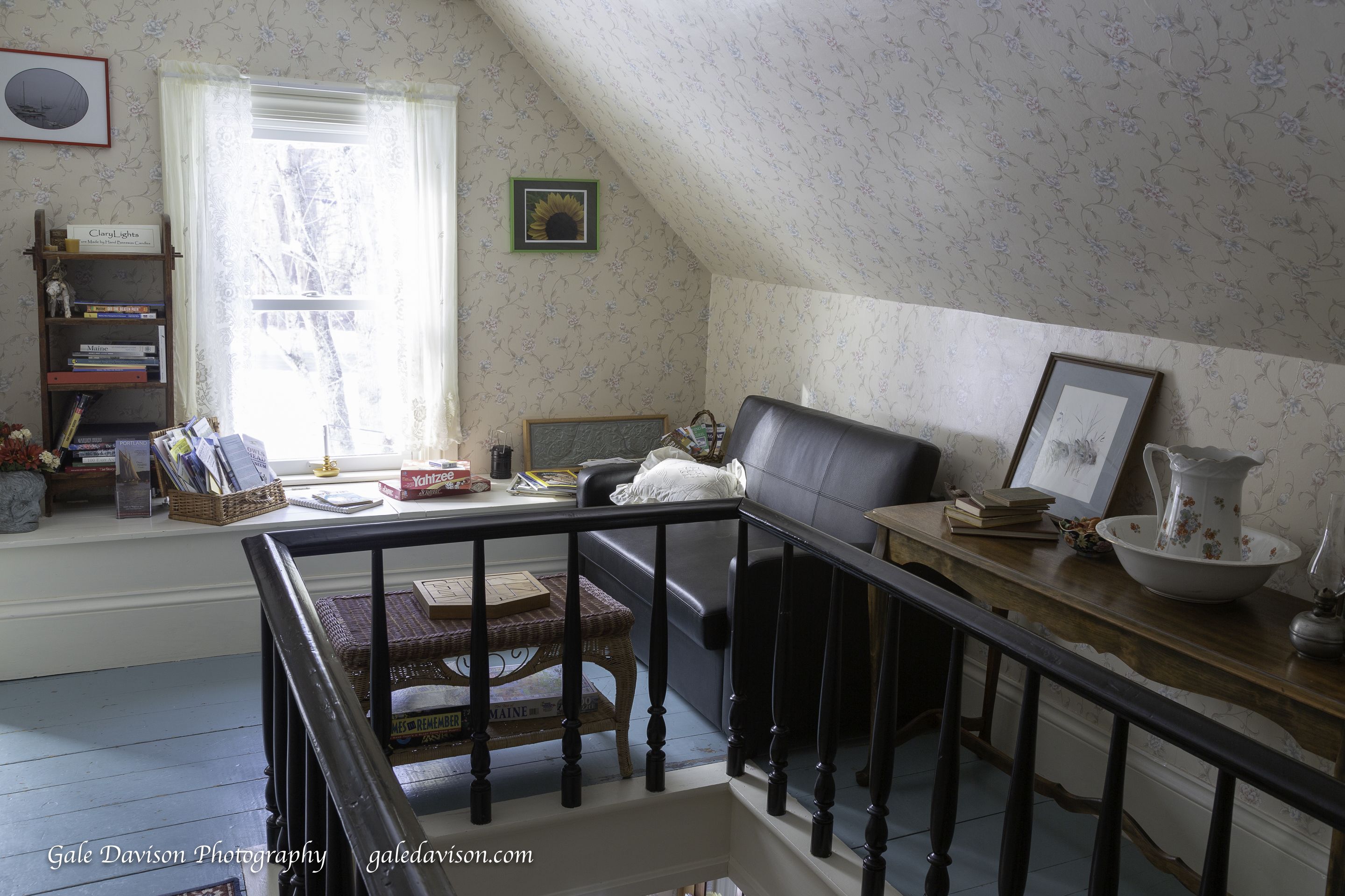 Una habitación acogedora con una escalera de madera, una estantería, un ventanal con papel tapiz floral y un sillón de cuero.