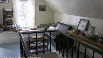 Una habitación acogedora con una escalera de madera, una estantería, un ventanal con papel tapiz floral y un sillón de cuero.