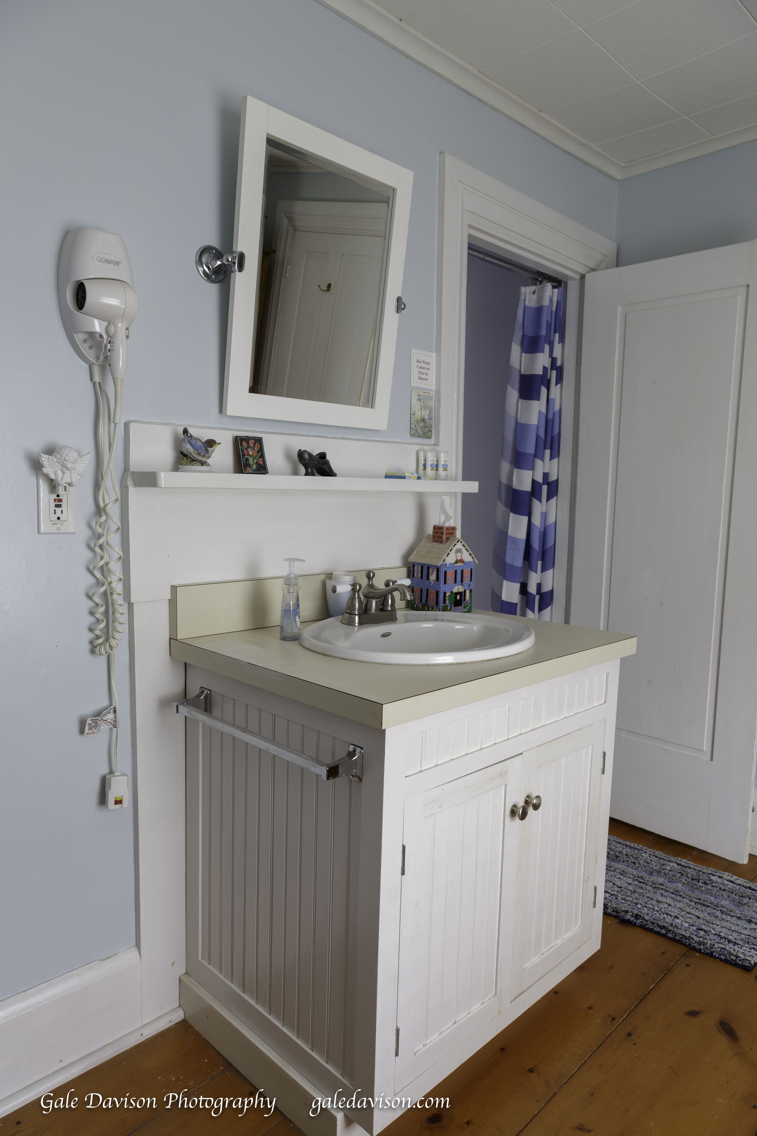 Une salle de bain avec un meuble-lavabo blanc, un miroir, un sèche-cheveux et un rideau de douche.