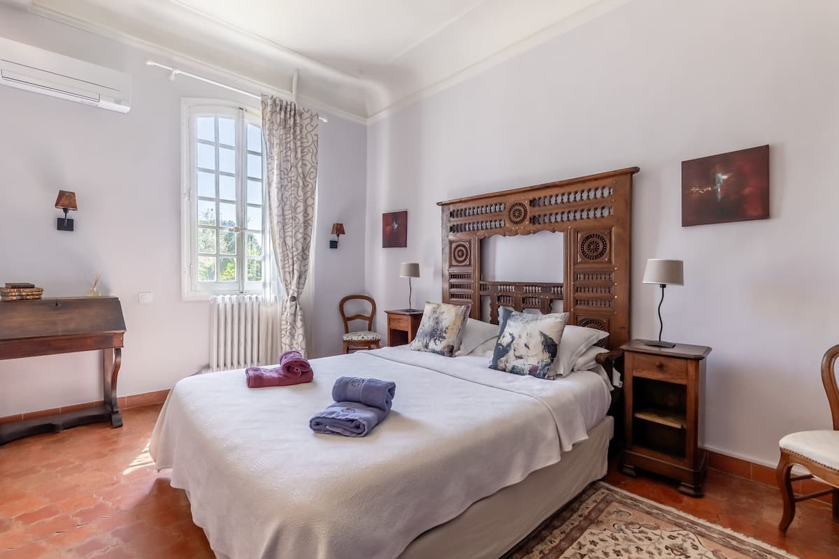 Quarto com cama grande, cabeceira de madeira, pequena escrivaninha, uma cadeira e radiador.