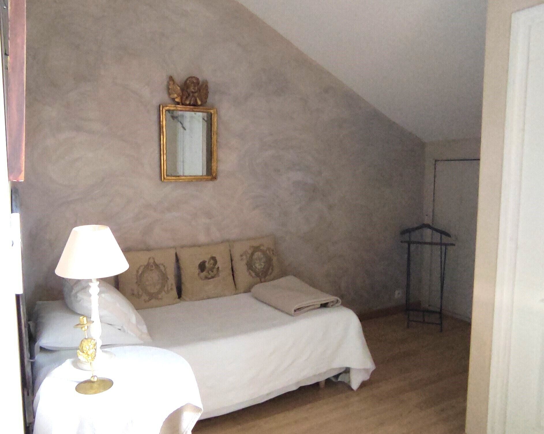 Un dormitorio con cama, mesita de noche, lámpara, espejo y perchero.