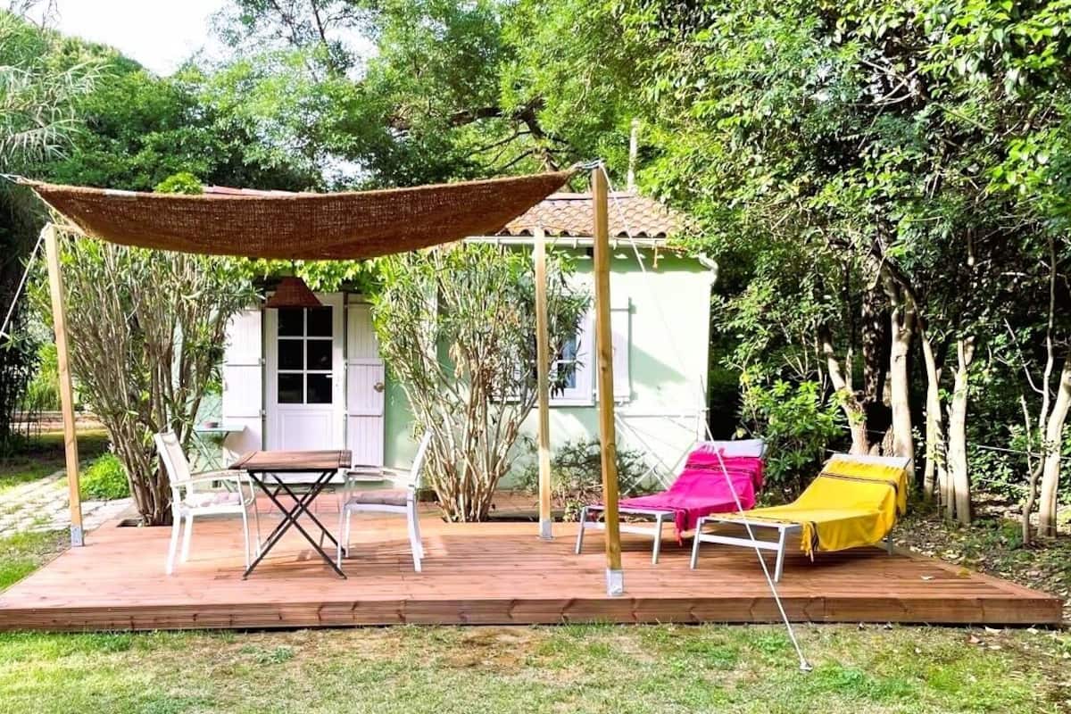 Um deck de madeira com toldo, duas cadeiras brancas e duas poltronas com capas amarelas e rosa.