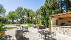 An outdoor patio with stone flooring, metal chairs, a glass table, and a stone wall. - Domaine de Rhodes (Avignon)