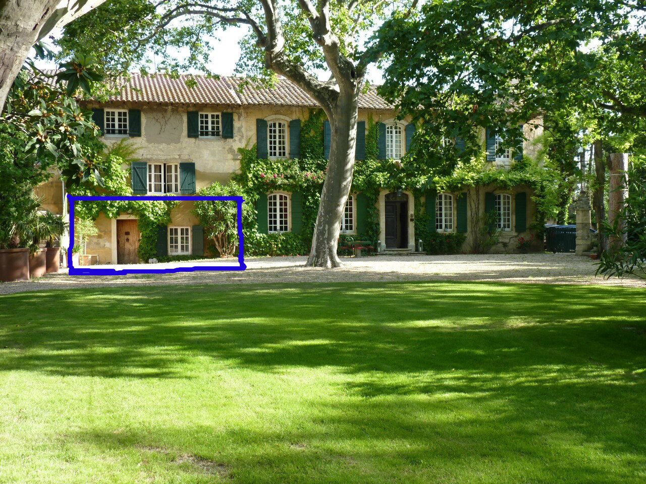 A traditional building with a tiled roof, green shutters, and a well-maintained lawn in front.