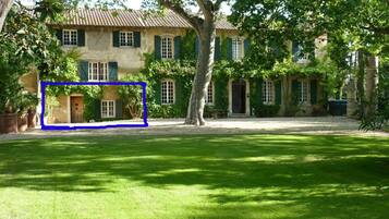 A traditional building with a tiled roof, green shutters, and a well-maintained lawn in front.