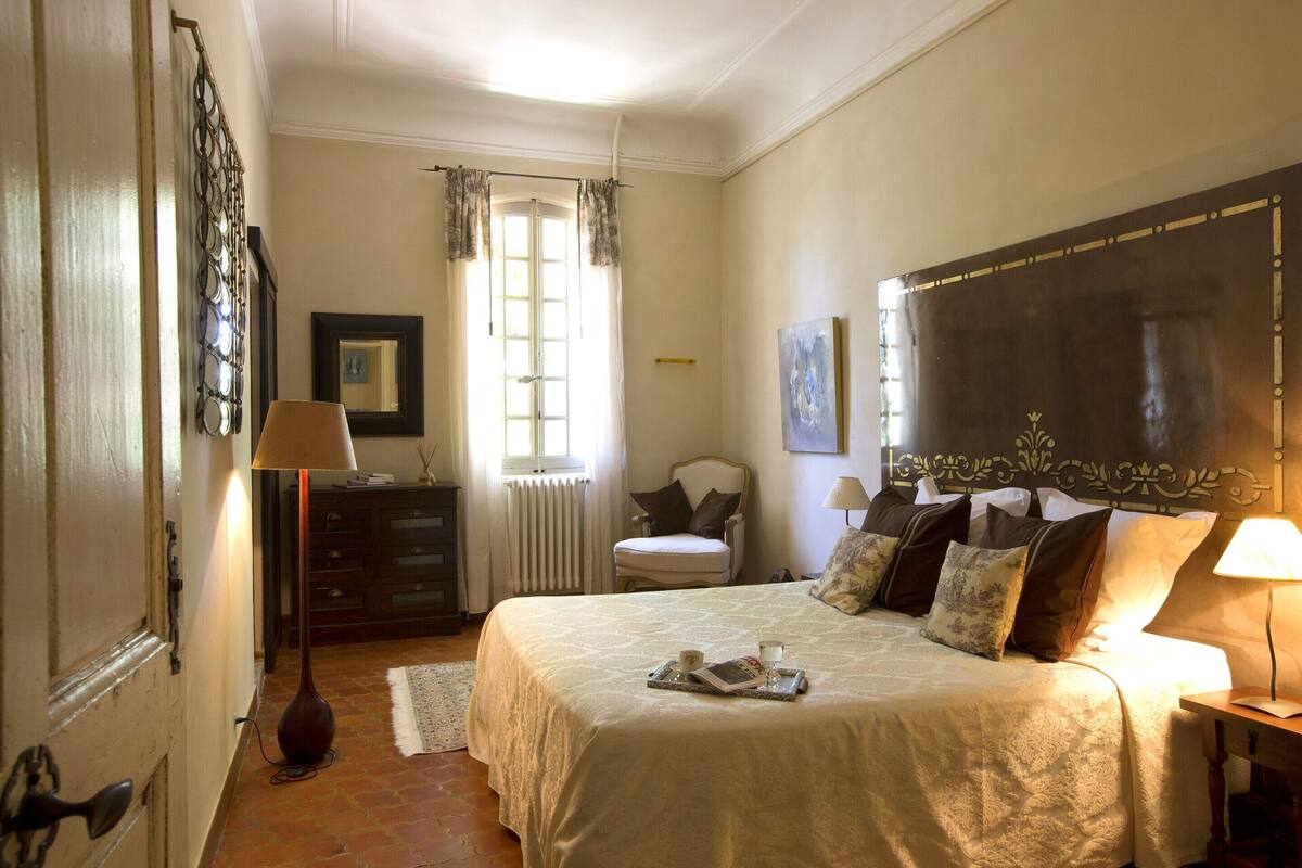 Quarto com uma cama grande, penteadeira, cadeira e janela com cortinas.