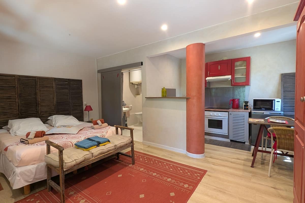 Quarto com cama de madeira, tapete vermelho, cozinha compacta com micro-ondas e armário vermelho.