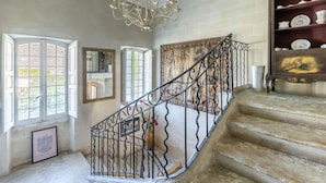 A grand staircase with ornate metal railings, a chandelier, and a collection of porcelain dishes on shelves. - Domaine de Rhodes (Avignon)