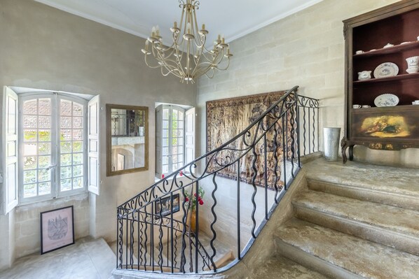 Una imponente escalera con barandales de metal ornamentados, un candelabro y una colección de vajilla de porcelana en estanterías.