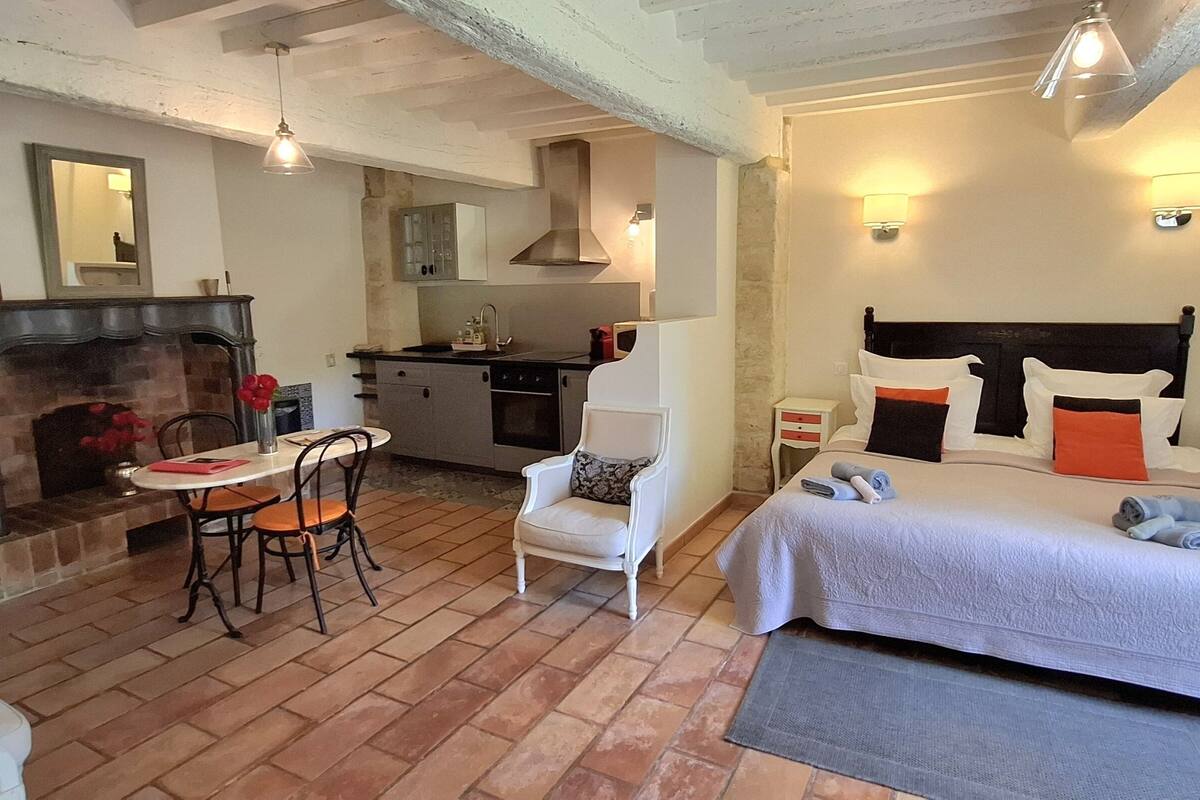 Um quarto aconchegante com lareira, mesa de jantar, cozinha e cama com almofadas.