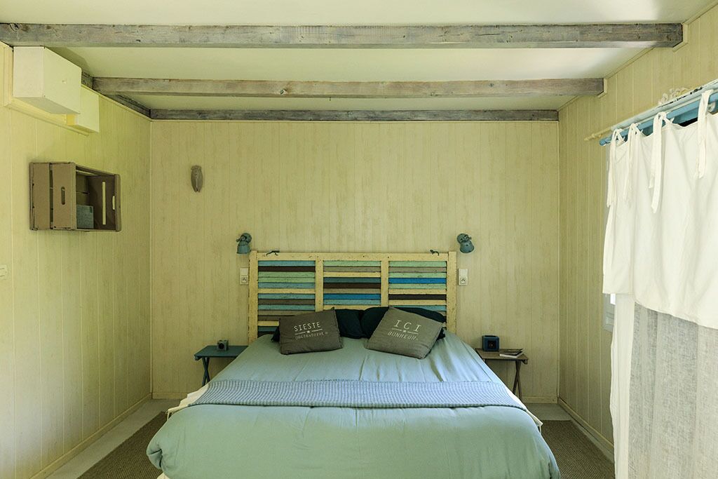 Een slaapkamer met een houten hoofdbord, een bed met een groene sprei, twee kussens, een nachtkastje en een klein tafeltje.