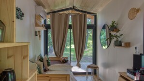 A cozy bedroom with a wooden bed, a small stool, a desk with a computer, and a large window with curtains. - Domaine de Rhodes (Avignon)