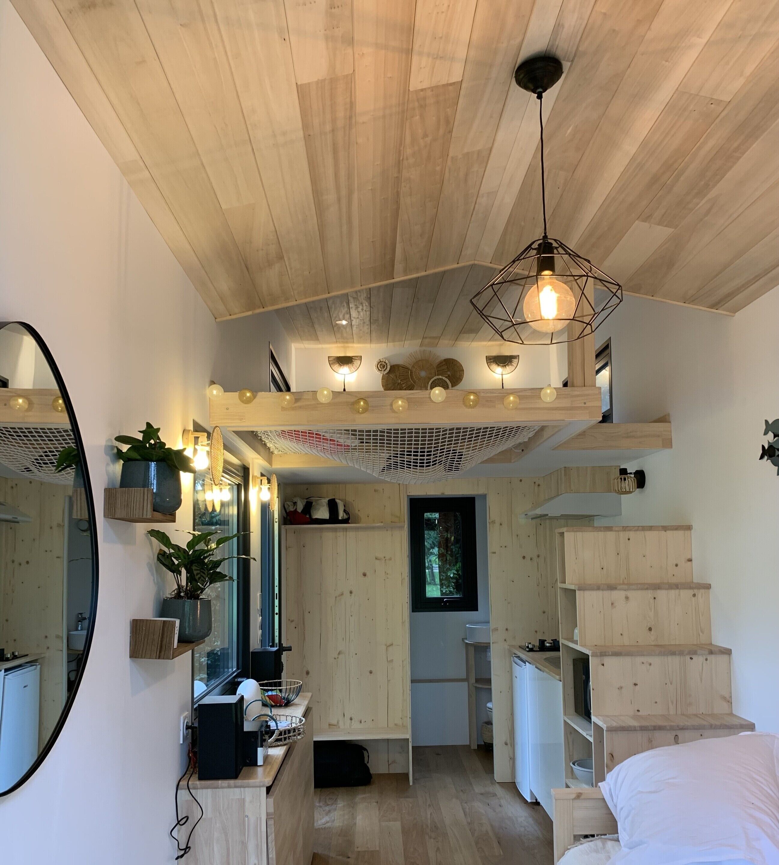 A compact bedroom with a wooden ceiling, a bed, a desk, and a mirror.