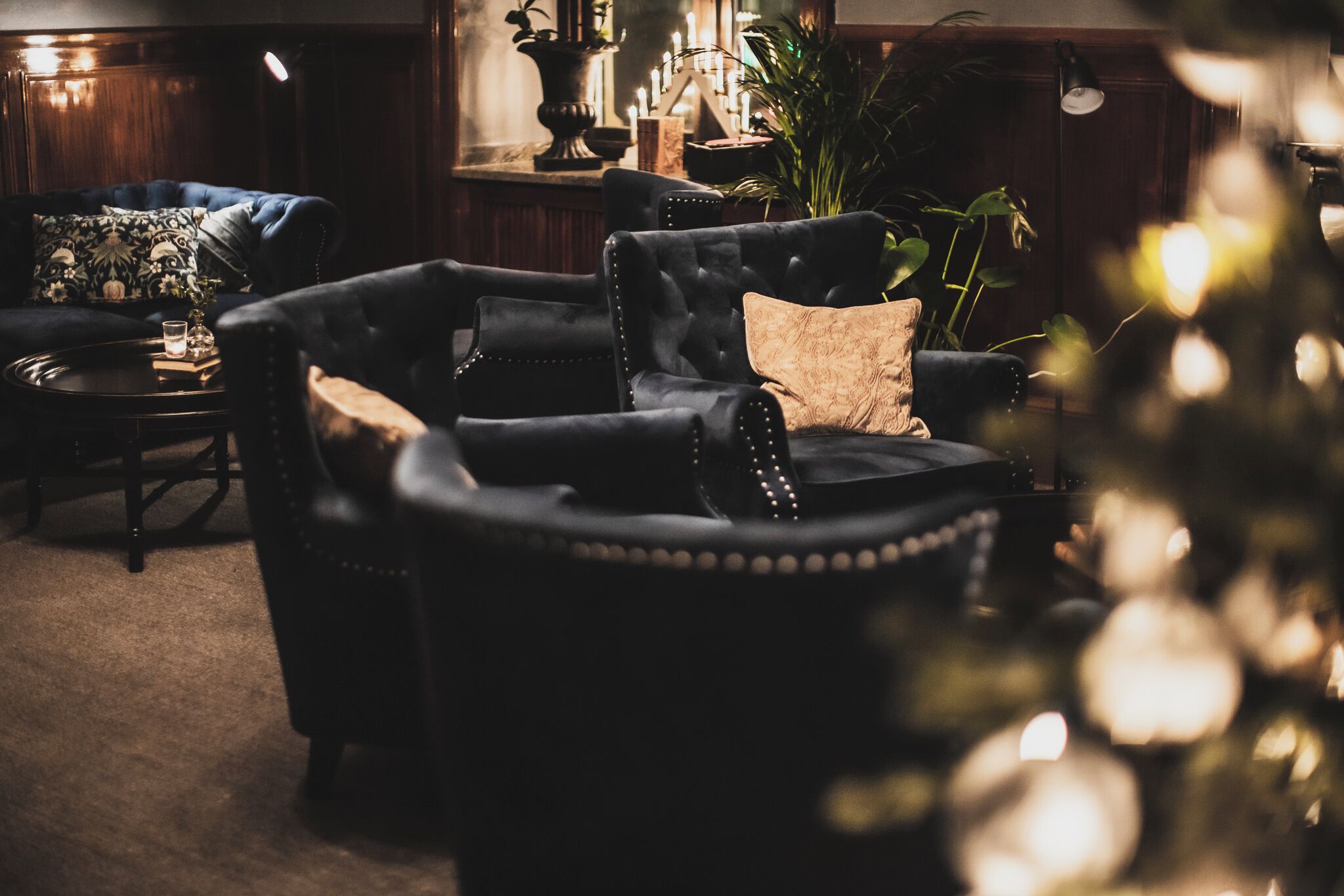 A dark wood-paneled room with a plush black armchair, a small round table, and a potted plant.