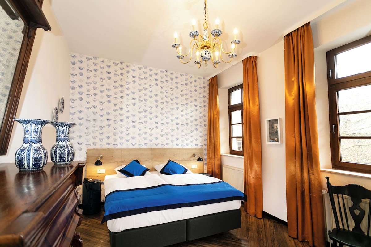 Un dormitorio con una cama grande, una araña, papel tapiz estampado y un ventanal con cortinas.