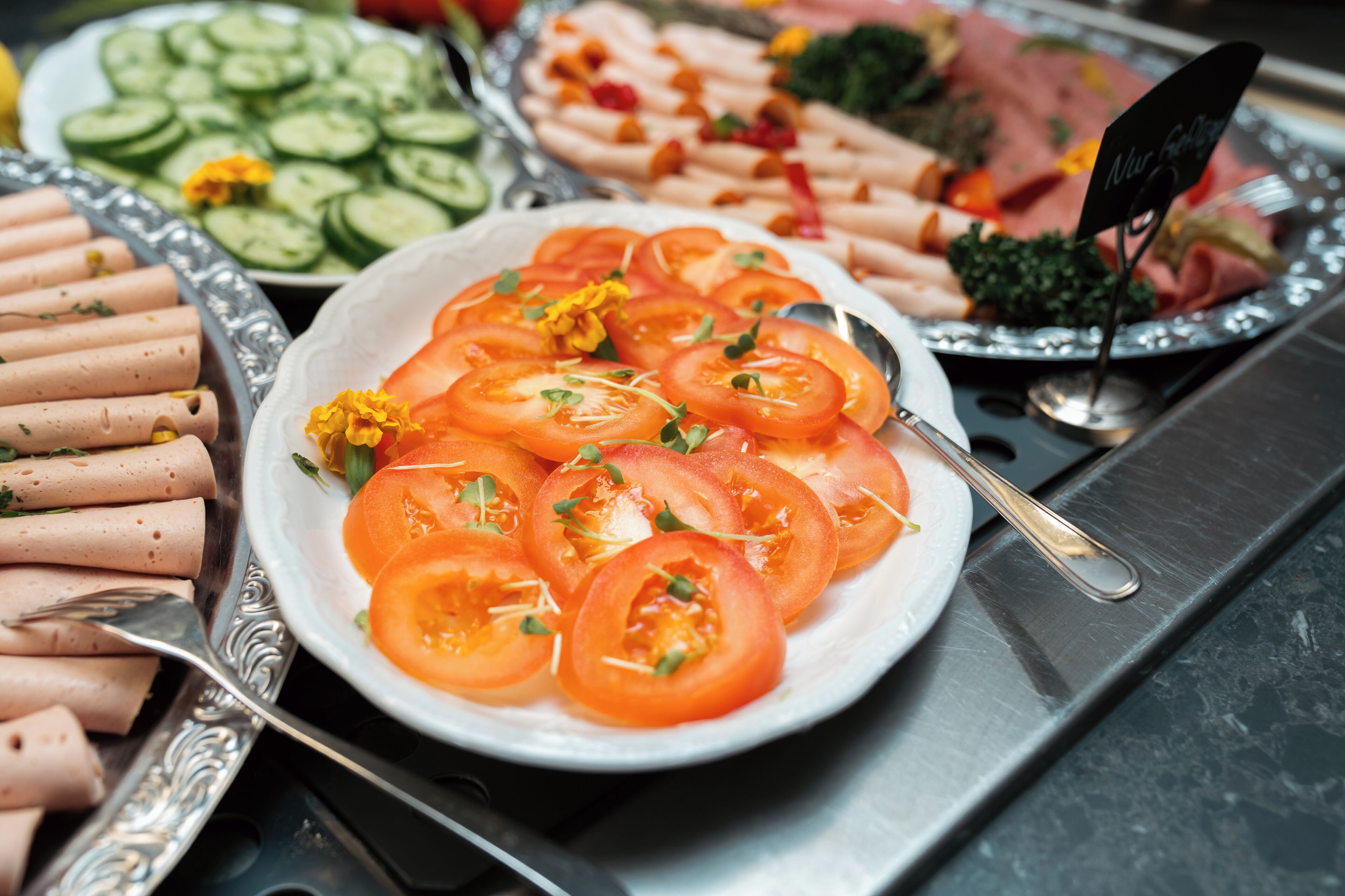 A buffet with various food items including sliced tomatoes, cucumbers, and meats.