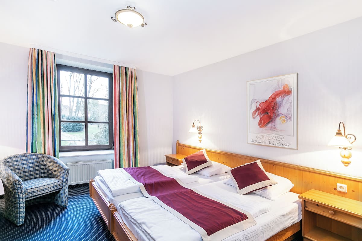Una habitación de hotel con una cama, una silla, una ventana con cortinas y un cuadro en la pared.