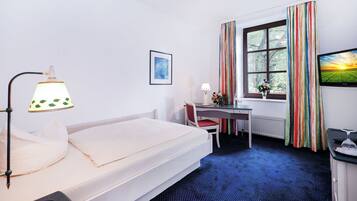 A hotel room with a bed, desk, chair, and a window with curtains.