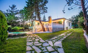 A two-story house with a stone pathway leading to a pool, surrounded by lush greenery. - Villa Euphoria (Thasos)