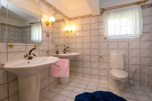 A bathroom with a sink, two mirrors, a toilet, and a window with a curtain.
