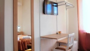 A bedroom with a wooden bed, a desk with a chair, a TV mounted on the wall, and a window with curtains. - Villa Achibea (Agrigento)