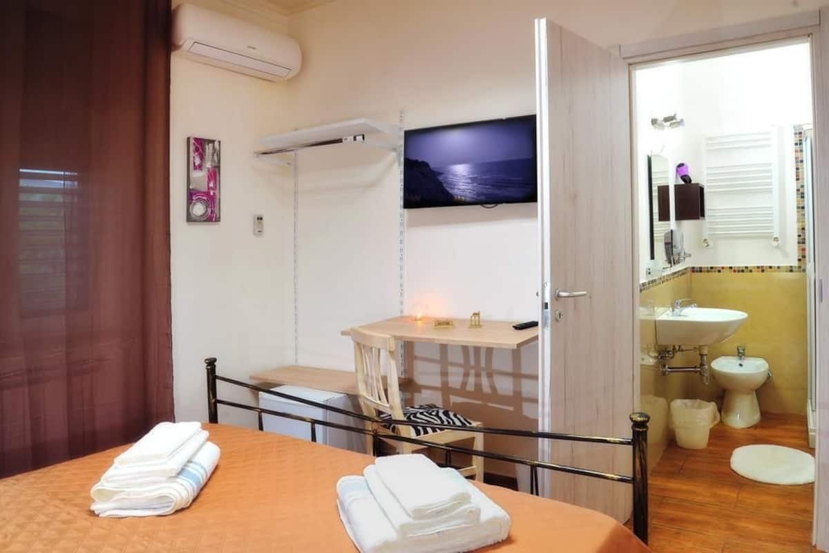 A hotel room with a bed, a desk, a TV, a bathroom with a sink and bidet, and a view of the sea.