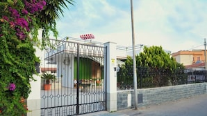 A gated entrance with a metal gate, a red and white striped umbrella, and a green door. - Villa Achibea (Agrigento)