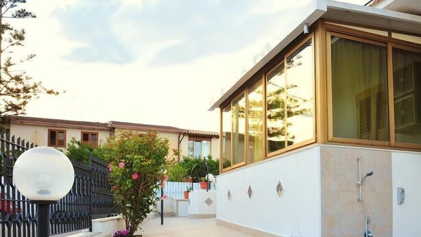 A modern house with a large glass window, a small garden with steps leading to the entrance, and a metal fence. - Villa Achibea (Agrigento)