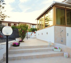A modern house with a large glass window, a small garden with steps leading to the entrance, and a metal fence. - Villa Achibea (Agrigento)
