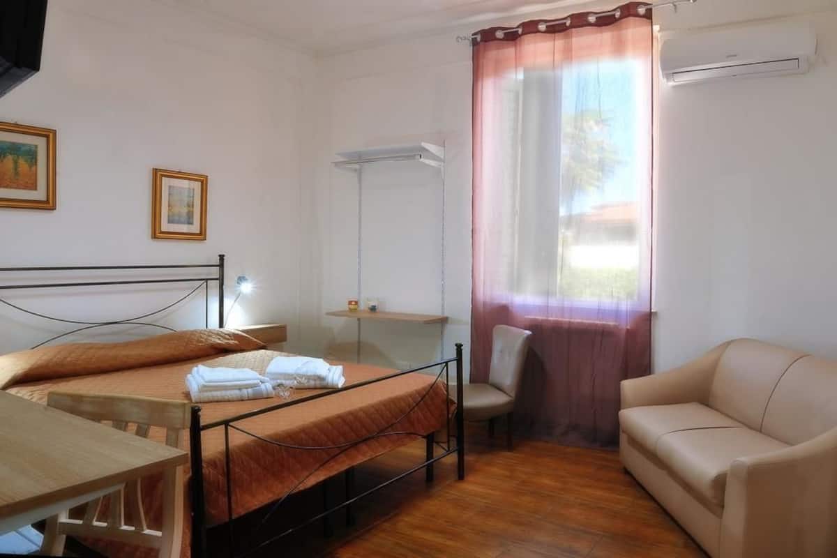 A hotel room with a bed, a desk, a chair, a sofa, and a window with curtains.