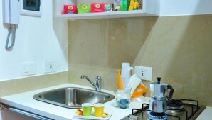 A compact kitchen with a sink, a stove, and a shelf above the sink holding various food items. - Villa Achibea (Agrigento)