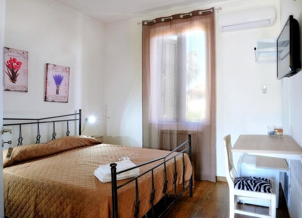 A bedroom with a bed, a desk, and a chair. There are two wall decorations and a window with curtains. - Villa Achibea (Agrigento)