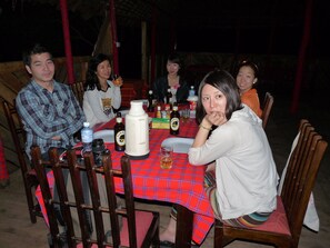 A group of people seated around a table with a red checkered tablecloth, wooden chairs, and various bottles and glasses on the table.