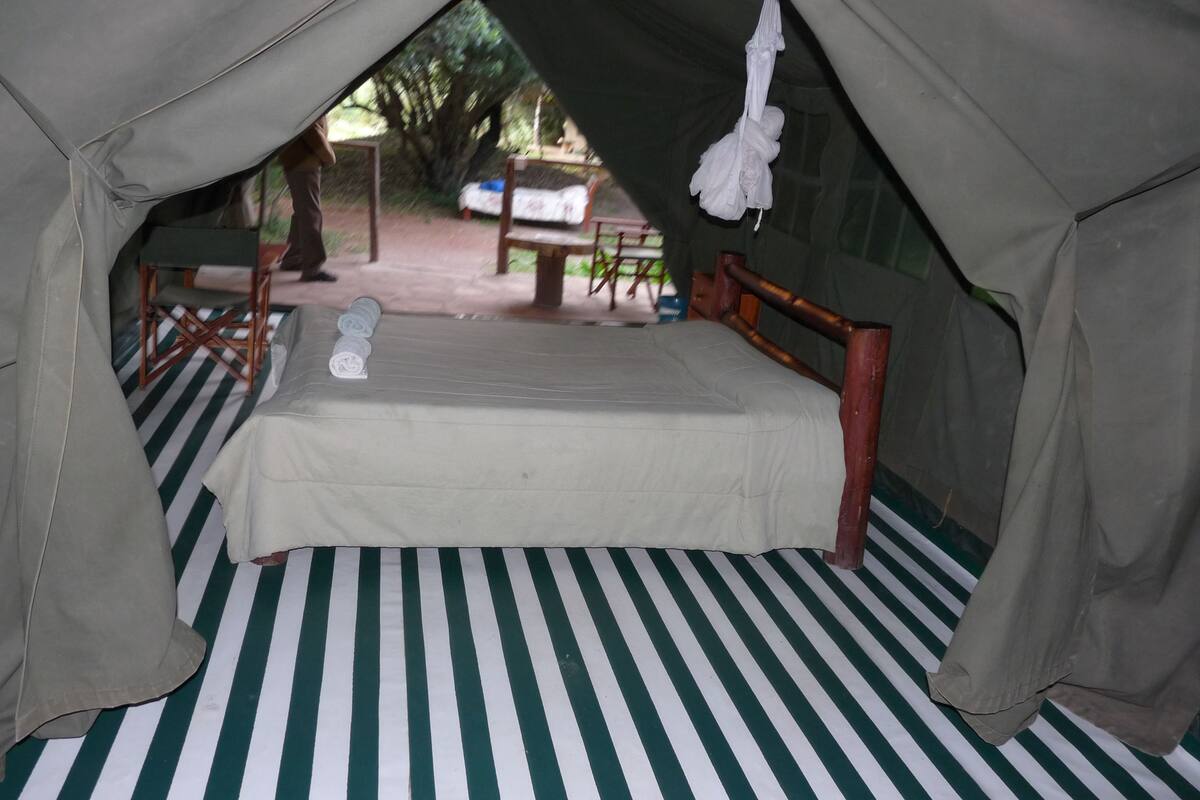 Tienda de campaña con una cama, piso a rayas y un banco afuera.