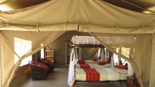 A tented accommodation with two beds, each with red and white bedding, and a wooden chest of drawers.