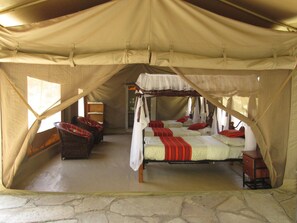 A tented accommodation with two beds, each with red and white bedding, and a wooden chest of drawers.