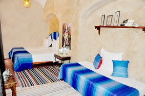 Habitación de hotel con dos camas, un tapete a rayas, una mesita con una lámpara y una repisa con marcos de fotos.