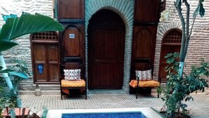 A swimming pool with a tiled edge, surrounded by a brick wall and wooden doors. - Riad Hidden (Marrakech)