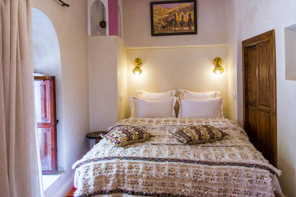 A bed with a patterned bedspread, two pillows, and wall-mounted lights.