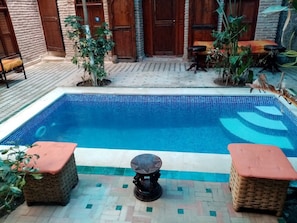 Una piscina con borde de azulejos, rodeada por un patio de ladrillo y puertas de madera.