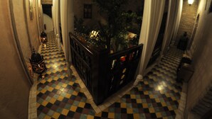 A narrow corridor with checkered flooring, a wooden railing, and a hanging plant. - Riad Hidden (Marrakech)
