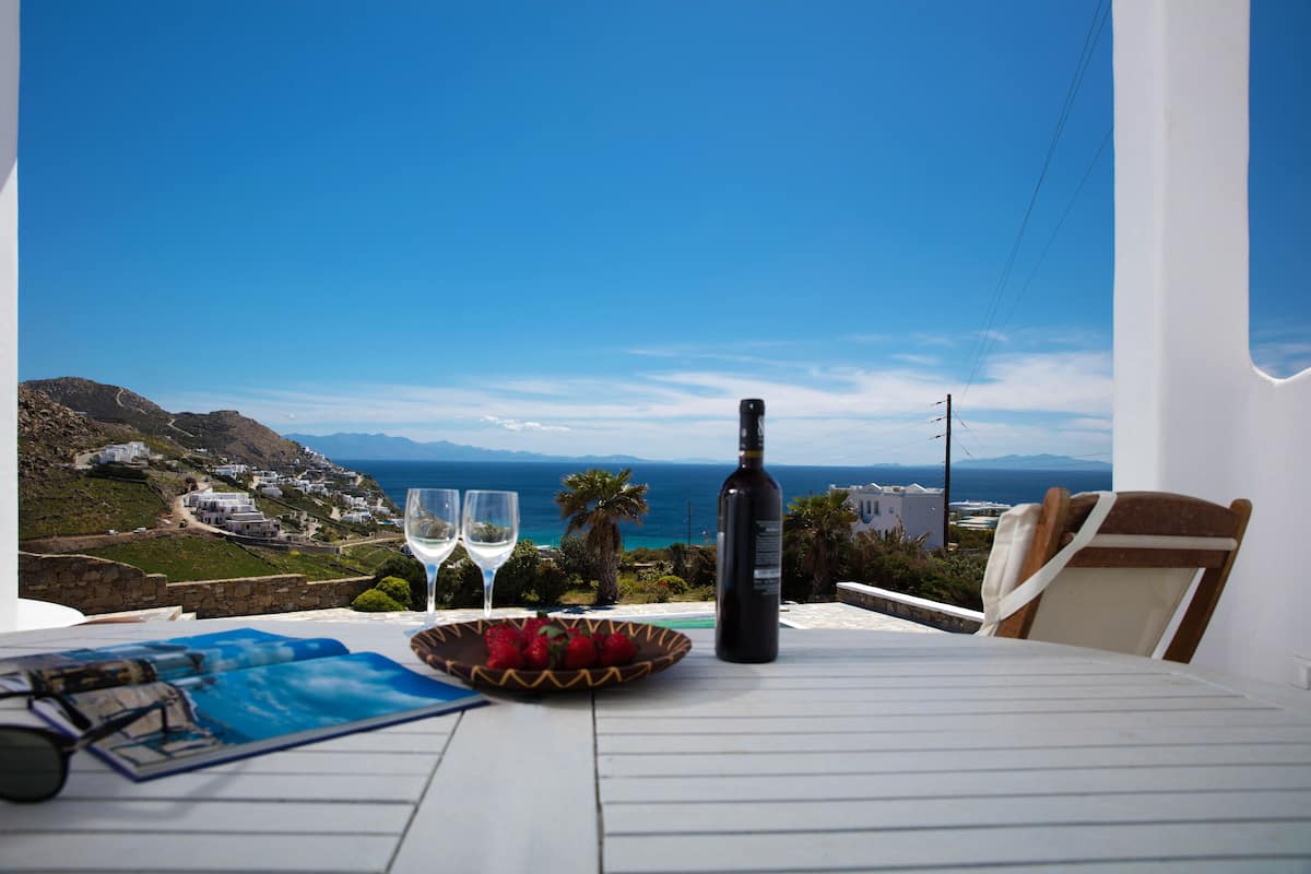 Une table avec une bouteille de vin, deux verres, un bol de fraises et une paire de lunettes de soleil.