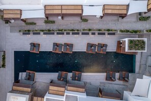 Luchtbeeld van een zwembad op een dak, met meerdere ligbedden en houten terras zitplaatsen.
