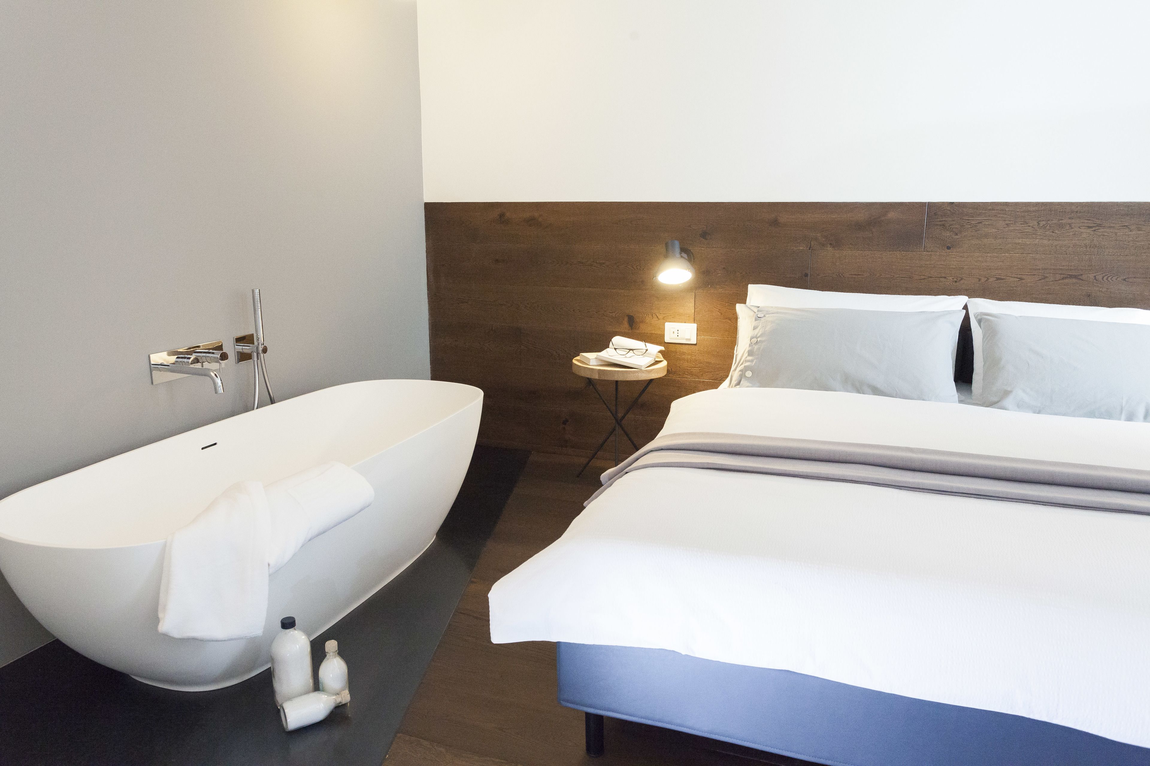 Un baño moderno con una bañera independiente, una mesita de noche con lámpara y una cama bien tendida.