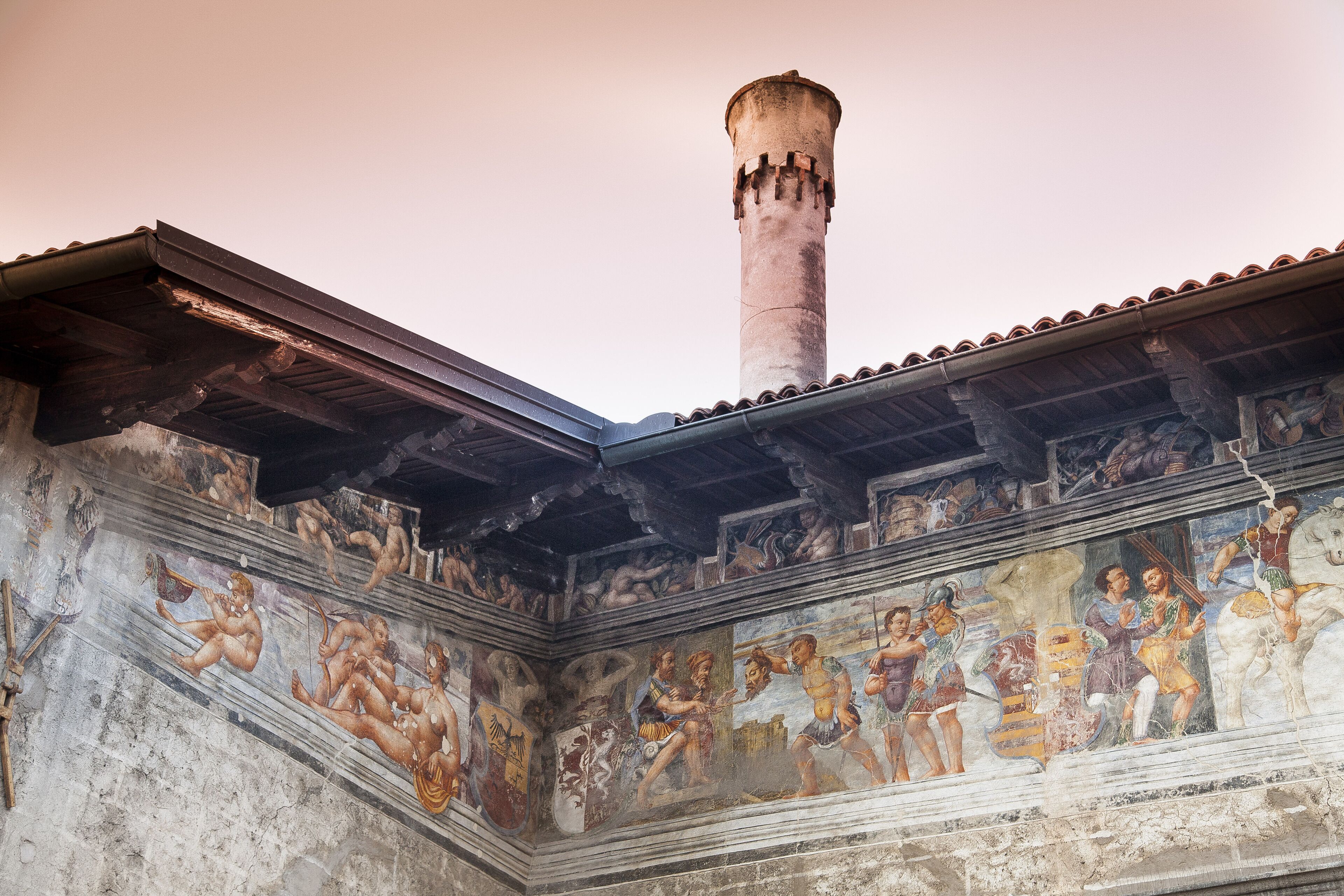 Ein historisches Gebäude mit einem hohen, zylindrischen Turm und einem Fresko, das klassische Figuren zeigt.