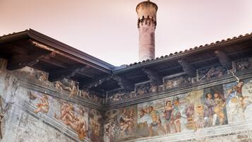 Ein historisches Gebäude mit einem hohen, zylindrischen Turm und einem Fresko, das klassische Figuren zeigt.