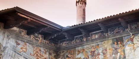 A historical building with a tall, cylindrical tower and a fresco mural depicting classical figures.